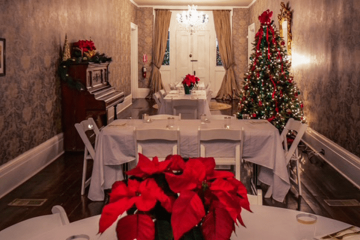 Festive room with a Christmas tree, poinsettias, and a piano, set for a gathering.
