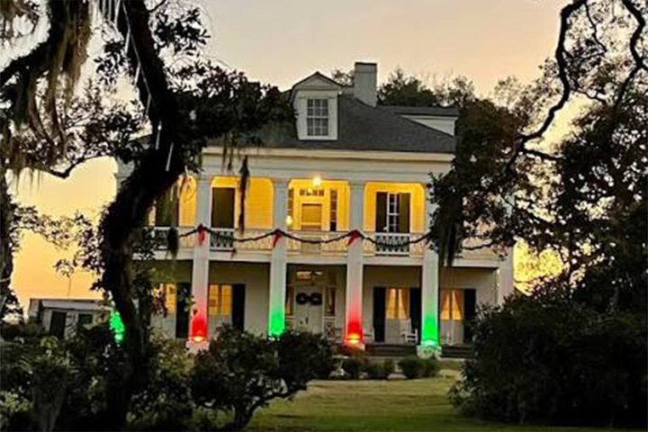A two-story house with columns, lit with red and green lights at dusk.