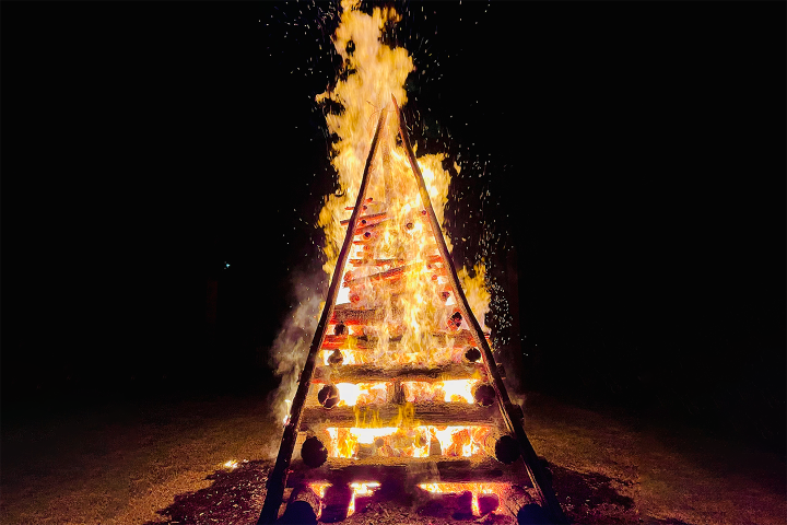 Triangular wooden structure engulfed in flames at night.