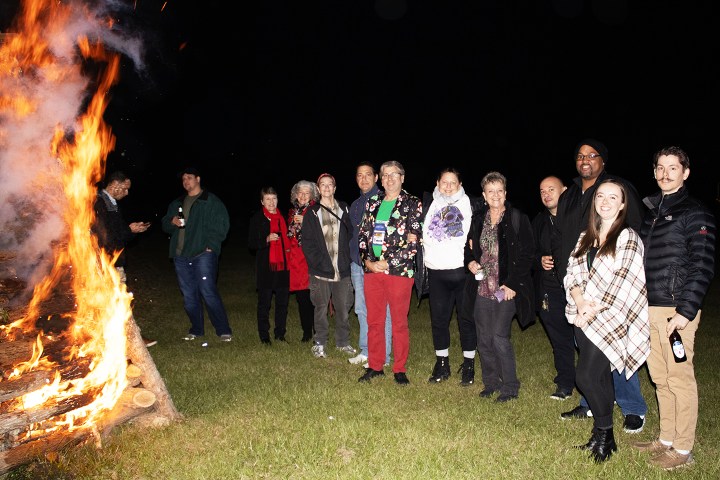 Group of people standing near a large outdoor bonfire at night.