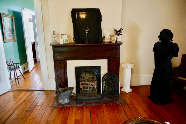 Vintage room with fireplace, framed photos, and a black-draped statue on the right.