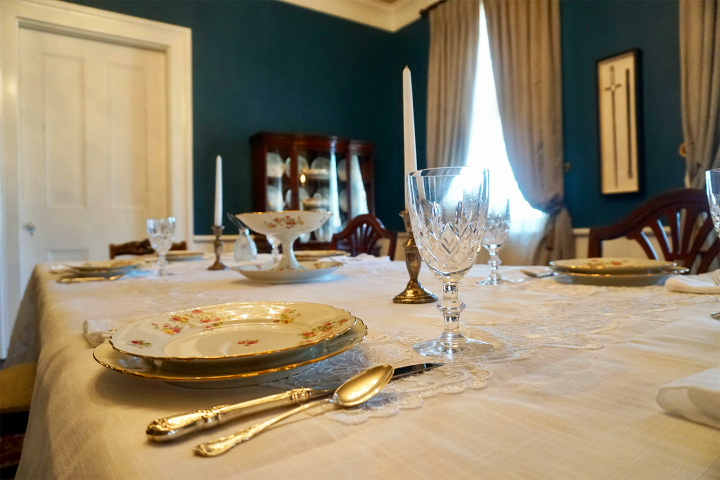 Elegant dining table with fine china and crystal glasses set for a meal in a room with blue walls.