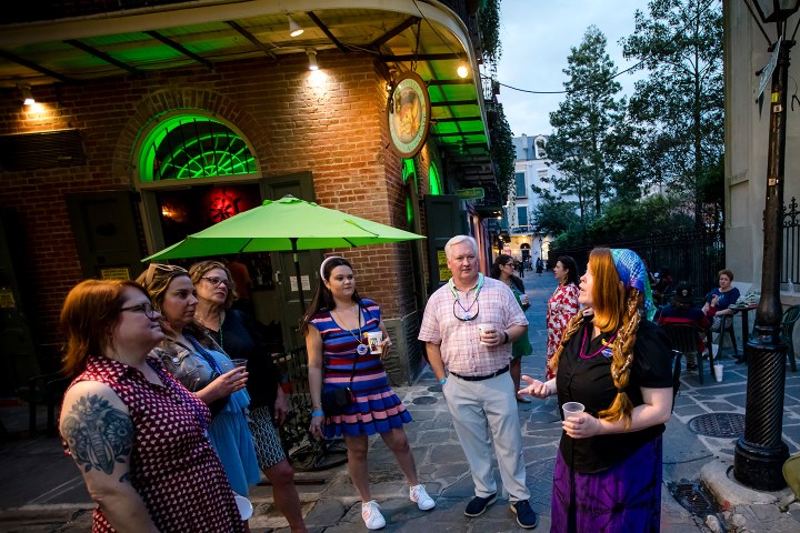 Group of people outside a building with green lights, some holding drinks, engaging in conversation.