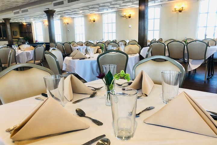 Elegant dining room with tables set for a banquet, featuring folded napkins and glasses.