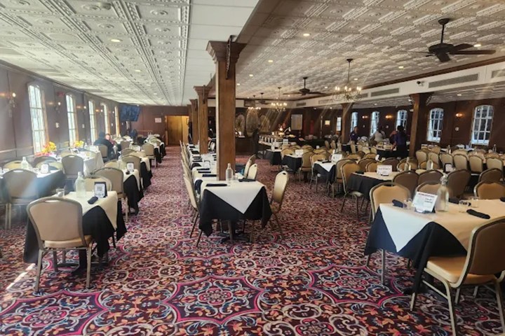 Large dining room with patterned carpet, set tables, and decorative ceiling panels.