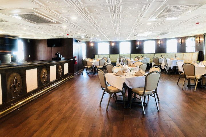 Elegant dining room with round tables, white tablecloths, and cushioned chairs on wood flooring.