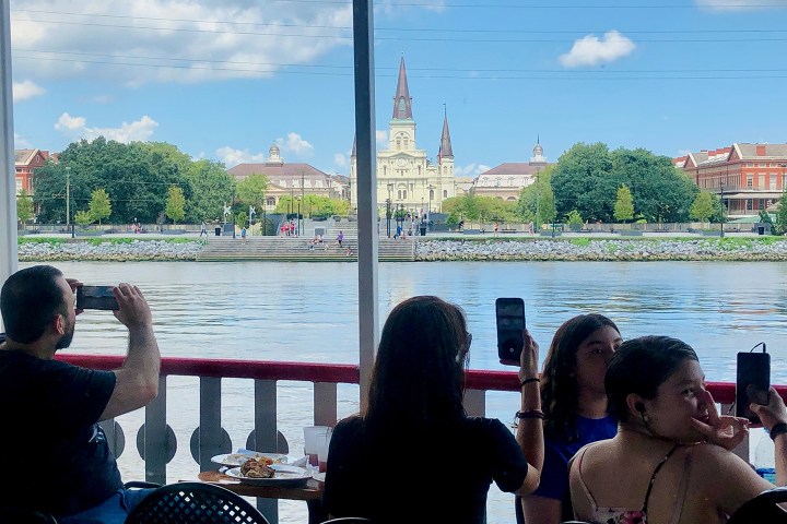 People taking photos from a boat with a cathedral and trees across the river.