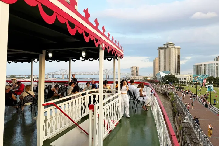 People relaxing on a riverboat deck with city skyline and bridge in the background.
