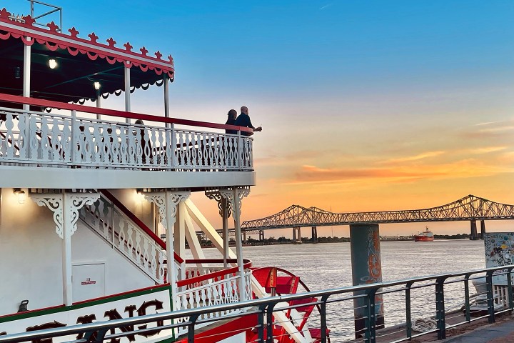 A steamboat on a river at sunset with a bridge in the background.