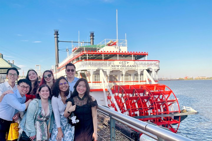 Group of people smiling in front of a riverboat with paddlewheel and 'City of New Orleans' sign.