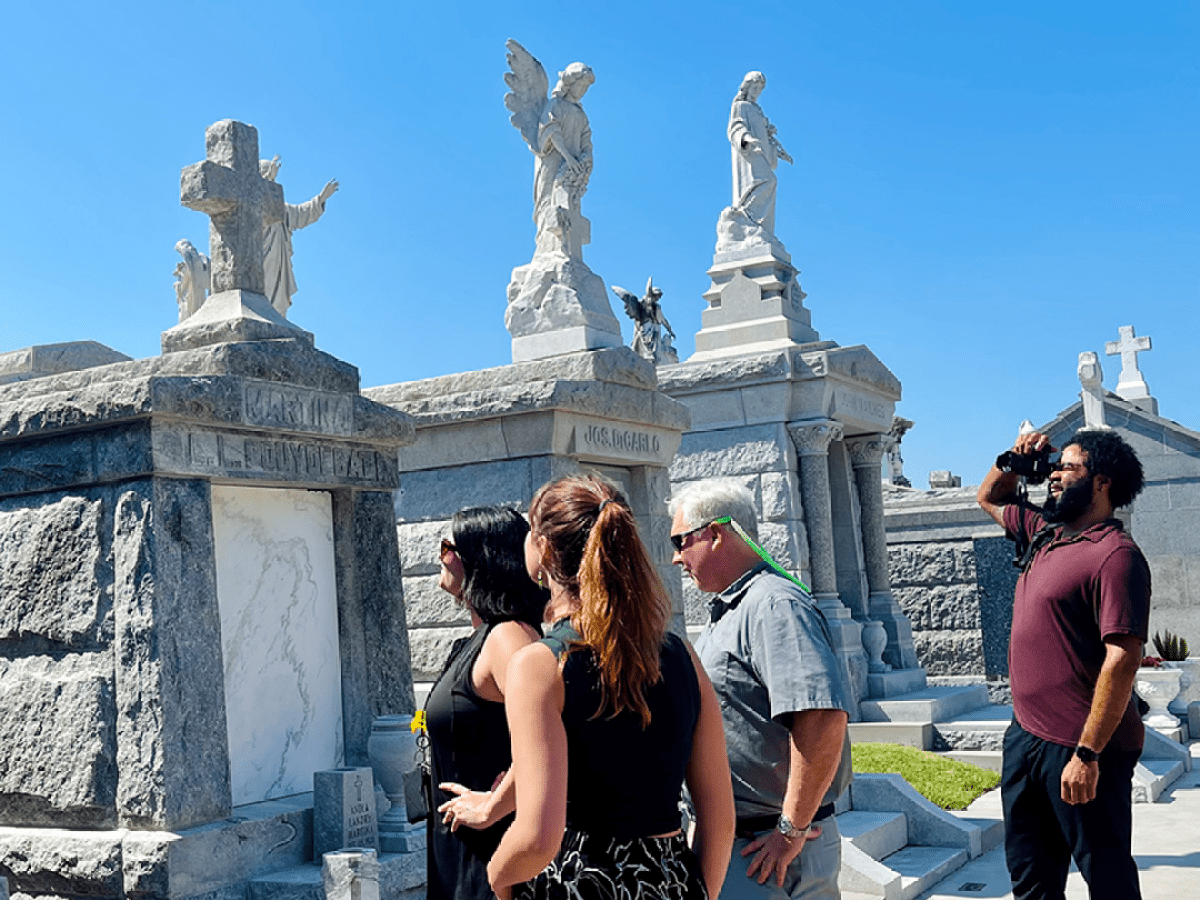 Group of people touring a cemetery with ornate stone tombs.