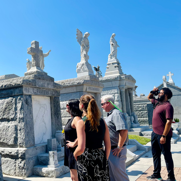 Group of people touring a cemetery with ornate stone tombs.
