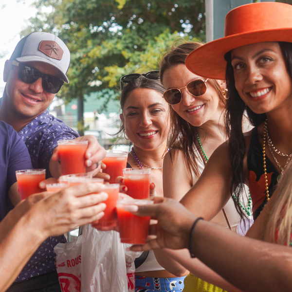 Group of people outdoors toasting with red drinks, wearing sunglasses and hats.