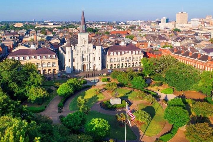 Aerial view of park with cathedral and buildings in background on a sunny day.