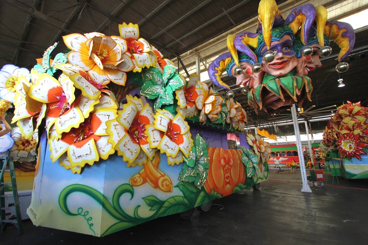 Colorful parade float with large flowers and jester heads in a warehouse.