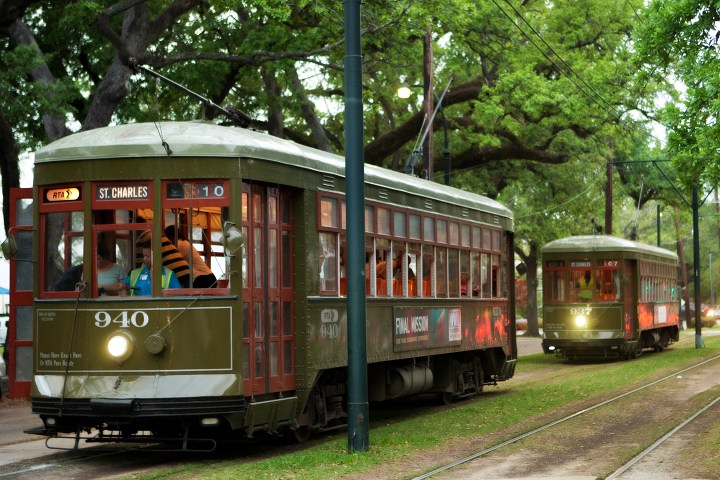 Two green streetcars on a tree-lined track, labeled St. Charles.