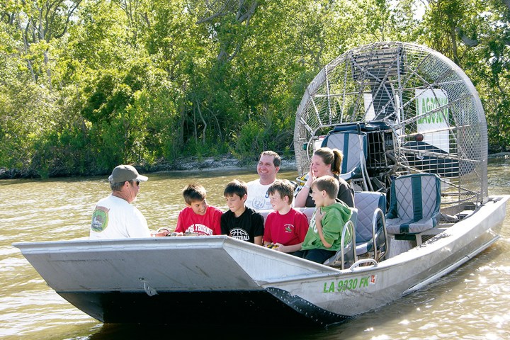 Group of people on an airboat ride in a swamp area with trees in the background.