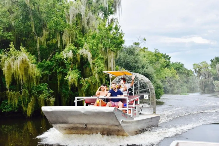 People riding an airboat on a river surrounded by trees.