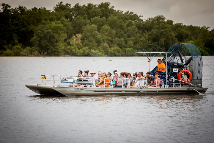Tourists on an airboat ride on a river, surrounded by trees.
